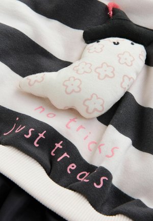 Randig tyg med svarta och vita horisontella linjer, med en mjuk spökliknande design och texten "inga trick, bara spår" i rosa.