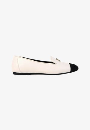 Chaussure plate blanche avec embout noir et petite décoration en chaîne dorée sur le dessus avant, vue de profil.