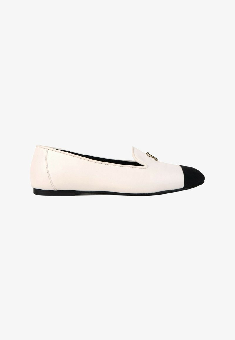 Chaussure plate blanche avec embout noir et petite décoration en chaîne dorée sur le dessus avant, vue de profil.