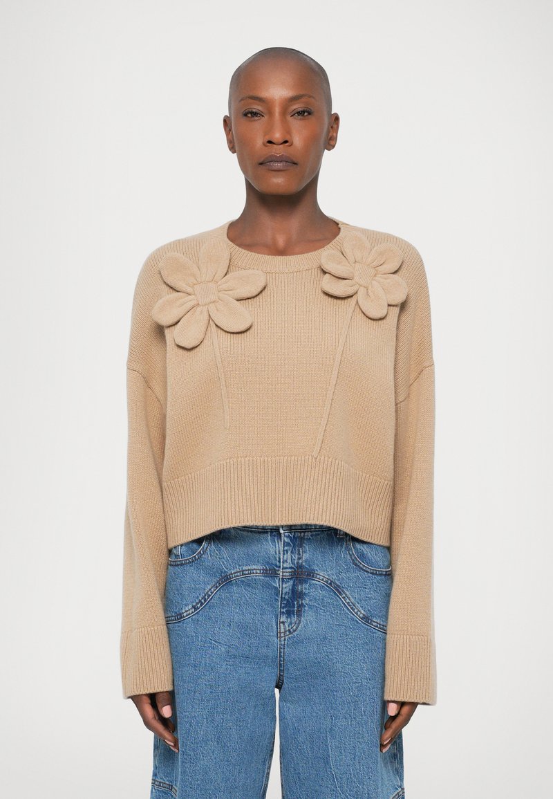 Pulover bej scurt, cu applique din tricot în formă de flori pe umeri, cu guler și margine ribbed, asortat cu pantaloni largi din denim albastru.