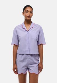 Ensemble de pyjama court de couleur violet clair à manches courtes, avec un liseré rouge festonné au niveau du col et des shorts, et une poche poitrine sur le haut.