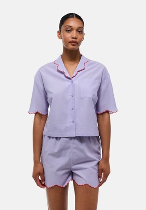 Ensemble de pyjama court de couleur violet clair à manches courtes, avec un liseré rouge festonné au niveau du col et des shorts, et une poche poitrine sur le haut.