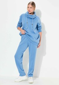 Sudadera con capucha azul claro, con cordones y bolsillos laterales, combinada con pantalones de chándal a juego que presentan un corte relajado y una textura suave.