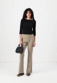 Black fitted top, beige tailored pants with side buttons, black textured handbag, leopard print slippers, standing against a plain background.
