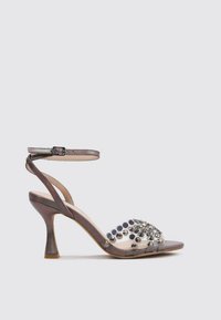 Sandale à talons hauts avec une bride avant transparente, ornée de clous argentés et noirs, bride de cheville marron et talon étroit texturé.
