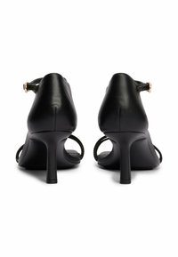 Scarpe nere in pelle con tacco alto, con tacco sottile, apertura sul retro e cinturino alla caviglia con fibbia dorata. Texture liscia, design minimale.