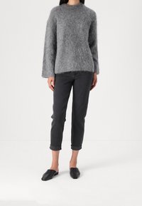 Grau flauschiger Pullover mit langen Ärmeln und Rundhalsausschnitt; kombiniert mit dunkelgrauen umgeschlagenen Jeans und schwarzen Slippern.