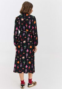 Czarna sukienka z kolorowymi, fantazyjnymi wzorami, długimi rękawami i wiązaniem w pasie. Noszona z czerwonymi skarpetkami i sneakersami w zwierzęcy wzór.