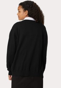 Czarny dzianinowy sweter z okrągłym dekoltem, ściągaczami na mankietach i u dołu, o luźnym kroju i gładkiej fakturze. Widok z tyłu.