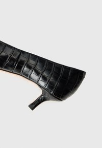 Black heeled shoe with a pointed toe, made of textured crocodile-patterned material, featuring a slim heel and smooth inner lining.