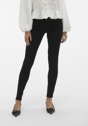 Black skinny jeans with a smooth texture, featuring a high waistband and tailored fit. Paired with pointed black heels.
