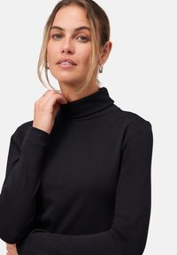 Musta poolpika kaelusega särk, mis on valmistatud pehmest kangast, veniv ja pikkade varrukatega. Sile tekstuur ja minimalistlik stiil.