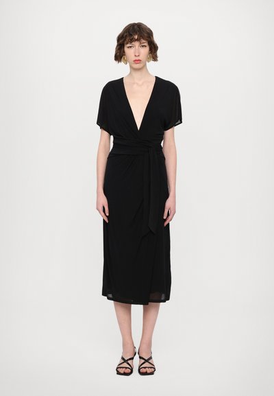 Vestido negro ajustado con escote en V profundo, mangas cortas y cinturón con lazo. Largo hasta la mitad de la pantorrilla, tejido ligero, textura suave y diseño minimalista.