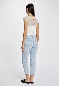White top with lace back, keyhole detail; light blue high-waisted jeans, tapered cut; worn with black slide sandals, minimal hardware.