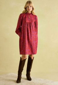 Flowy pink dress with floral pattern, keyhole neckline, and puff sleeves, paired with tall brown suede boots. Smooth texture and relaxed fit.