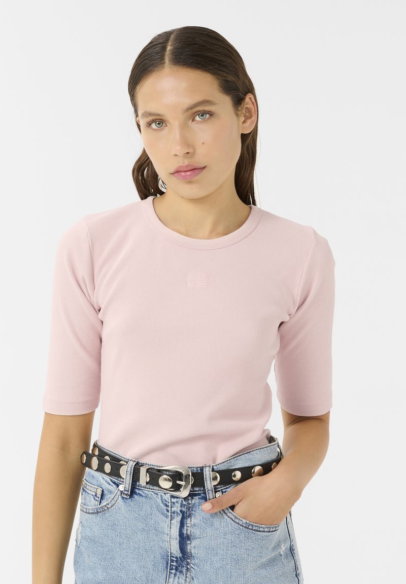 Light pink ribbed short-sleeve top with a round neckline; paired with high-waisted denim shorts and a black studded belt.