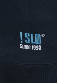 Mørkeblå sweatshirt med broderet tekst i lys blå og hvid: "!SLD Since 1993." Blødt stof med ribbet kant og manchetter.