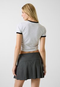 Szary krótki t-shirt z czarnym obszyciem zestawiony z plisowaną szarą spódnicą. Spódnica ma poziome linie i dopasowany pas.