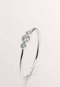 El anillo de plata presenta tres diamantes redondos de diferentes tamaños engastados en una delicada banda, mostrando un acabado pulido y suave.