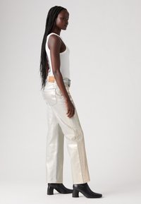 Jeans larghi color argento metallizzato con cuciture blu, abbinati a un top aderente bianco e stivali neri con tacco alla caviglia.