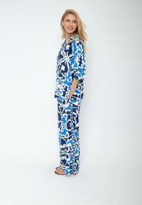 Twee-delige lounge set met een blauw-witte bloemenpatroon, bestaande uit een losvallend bovenstuk en wijde broekspijpen. Zachte, lichte stof.