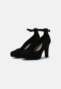 Černé semišové boty na vysokém podpatku s kulatou špičkou a páskem kolem kotníku, které mají masivní podpatek a vykrojené boky pro elegantní siluetu.