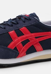 Sneakers con tomaia in rete blu navy, dettagli e sovrapposizioni in pelle rossa, lacci tondi e una suola imbottita bianca e beige.