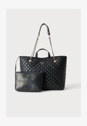 Borsa tote nera trapuntata con tracolle a catena dorata e piccola pochette abbinata con cerniera e logo GUESS su sfondo semplice.