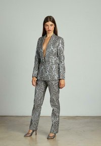 Completo floreale argento e nero con blazer a profondo scollo a V e pantaloni dritti, abbinato a scarpe con tacchi alti coordinate.