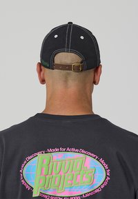 Fekete sapka barna állítható pánttal és fehér varrással. A póló színes grafikát tartalmaz zöld és rózsaszín szöveggel.