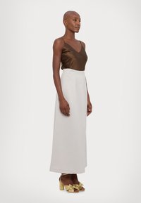 Brun sateng cami, høyt liv kremfarget skjørt og gull hælede sandaler med sløyfedetaljer. Glatte teksturer og elegant silhuett.