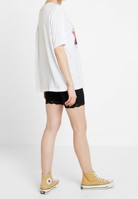 Vit oversized t-shirt med grafiskt tryck, kombinerad med svarta shorts med spetsdetaljer och ljusbruna högskurna sneakers.