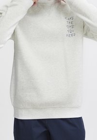 Jasnoszary sweter z miękkiego materiału z okrągłym dekoltem, z haftowanym napisem w granatowym kolorze: "WEŹ CZAS, KTÓRY POTRZEBUJESZ."