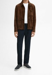 Brown suede jacket with front pockets, white t-shirt, dark trousers, and grey sneakers. Minimalist design with a relaxed fit.