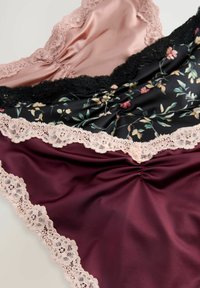 Drie stoffen van lingerie: zacht roze satijn met kant, zwart bloemen satijn met donker kant, en dieprode satijn met een lichte kantafwerking.