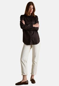 Black button-up shirt with small, multicolored dots, long sleeves, paired with white loose-fit pants and brown loafers.