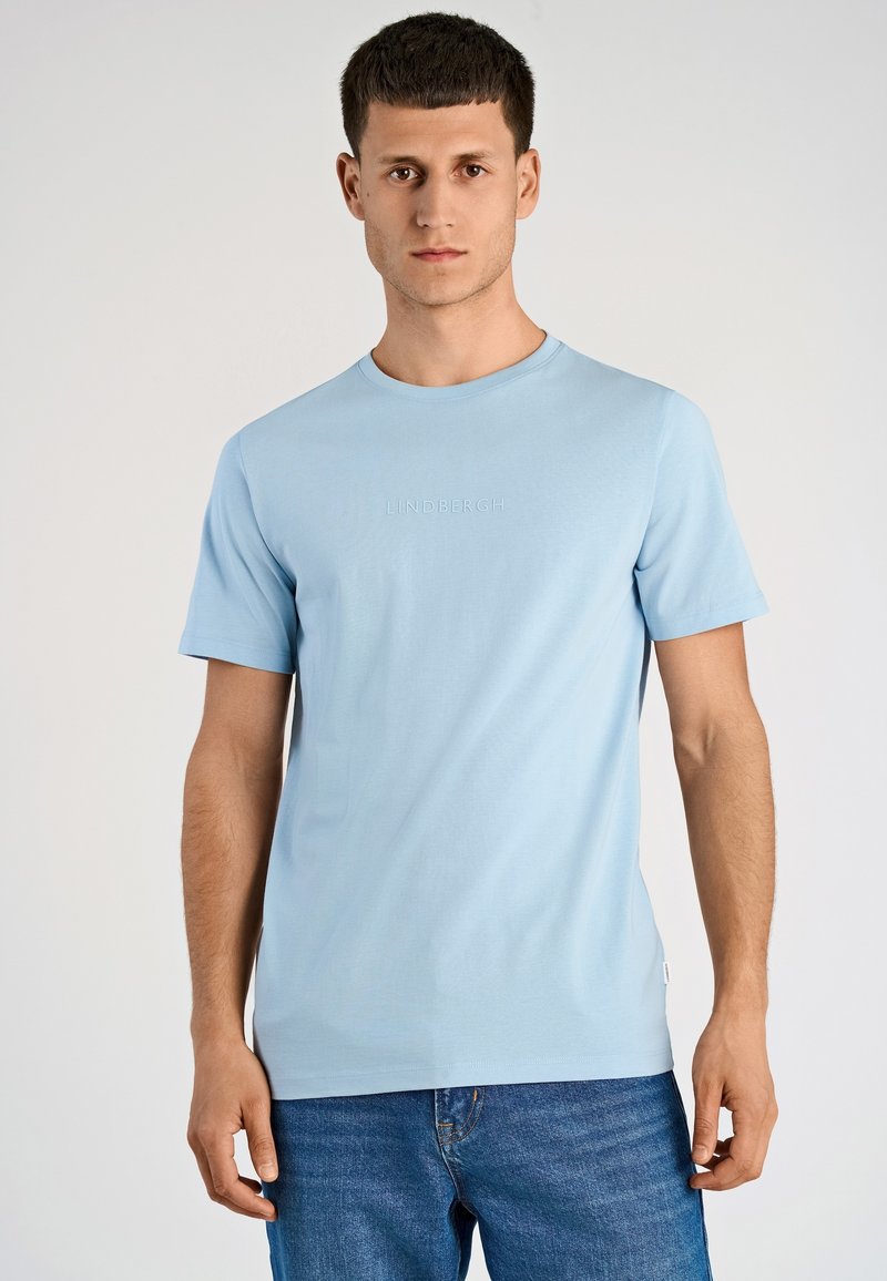 T-shirt in cotone azzurro chiaro con scollo rotondo e maniche corte. Presenta un logo in rilievo sul petto e un dettaglio con etichetta laterale. Perfetta per un abbigliamento casual.