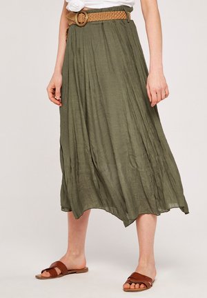 Długa spódnica w kolorze oliwkowej zieleni wykonana z lekkiego materiału, z plisami i surowym wykończeniem, zestawiona z plecionym paskiem i brązowymi sandałami na płaskim obcasie.