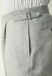 Pantalones grises ajustados con una tela texturizada, que presentan lazos para cinturón, plisados y un bolsillo lateral, acentuados por una hebilla de metal.