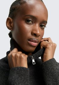 Czarny wełniany golf z zamkiem, z teksturowanym materiałem i prążkowanymi mankietami, które zwiększają ciepło i komfort.