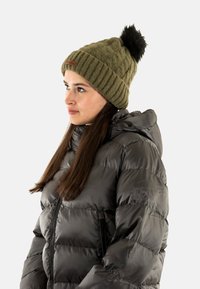 Gorro de punto verde oliva con un pompón negro, combinado con una chaqueta acolchada negra brillante que cuenta con cierre de cremallera y capucha.