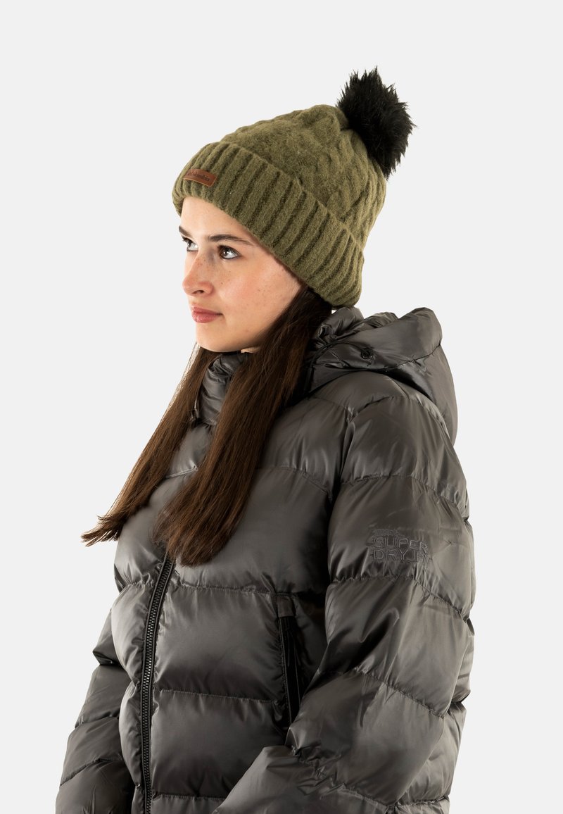 Gorro de punto verde oliva con un pompón negro, combinado con una chaqueta acolchada negra brillante que cuenta con cierre de cremallera y capucha.