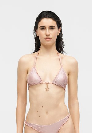 Woman with wet dark hair wearing a light pink shimmery bikini with star-shaped charms on top and bottom against a white background.