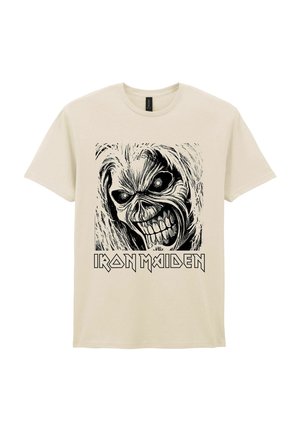 Camiseta beige con un gráfico en blanco y negro de una calavera sonriente y el texto "Iron Maiden" debajo de la imagen.