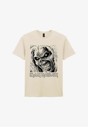 Beige T-shirt met een zwart-witte afbeelding van een grijnzend schedelgezicht en de tekst "Iron Maiden" onder de afbeelding.