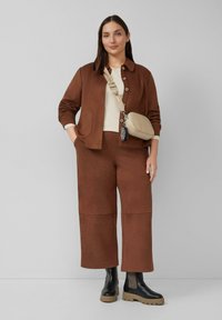 Bruine textuurjas met twee zakken, gecombineerd met bijpassende cropped broek. Korte crèmekleurige top eronder. Bruine en zwarte enkellaarsjes.