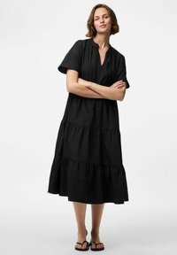 Must mustriga mustriga mustriga, millel on lühikesed varrukad, V-kaelus ja kogutud vöökoht, mis loob lõdva silueti.