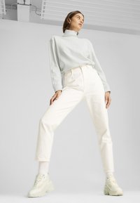 Top azul claro de manga larga y cuello alto, combinado con jeans blancos de pierna recta de tiro alto y zapatillas blancas gruesas. Texturas de tela suaves.