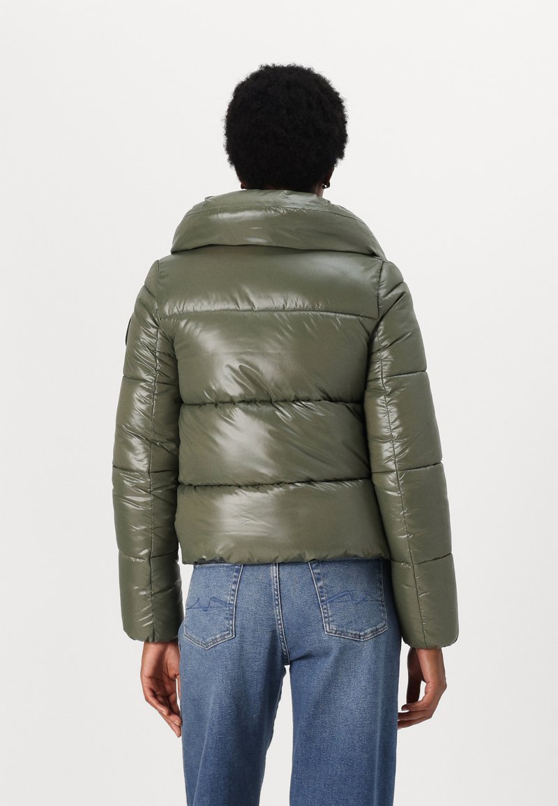 Grüne Pufferjacke mit glänzender Oberfläche, tailliertem Design, weitem Kragen, horizontalem Steppmuster und enger Passform, kombiniert mit blauen Jeans.