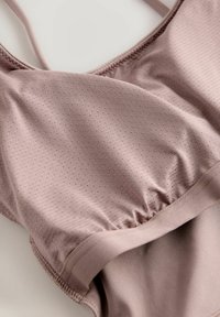 Brassière de sport mauve clair avec une surface texturée, dotée de fines bretelles et de coutures froncées, offrant un design respirant pour le confort.